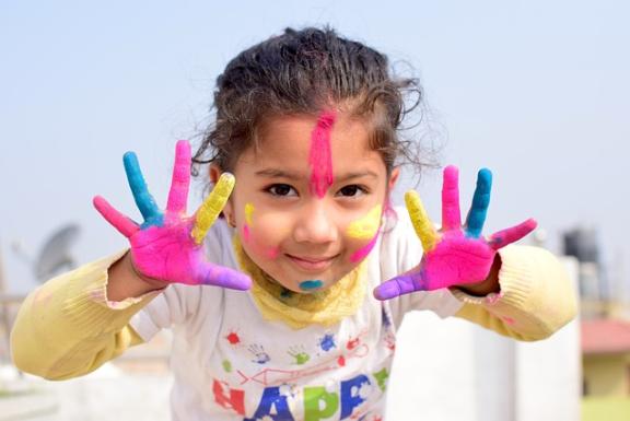 Young female child with colourful paint on hands and face