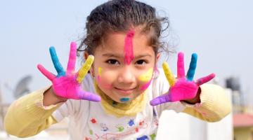 Young female child with colourful paint on hands and face